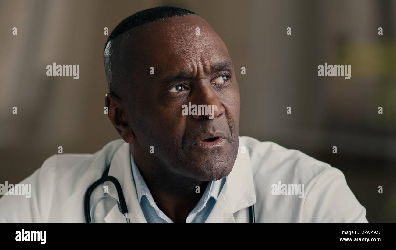 Puzzled thoughtful senior male professional medic mature adult doctor african american man in medical coat planning idea brainstorming thinking Stock Photo