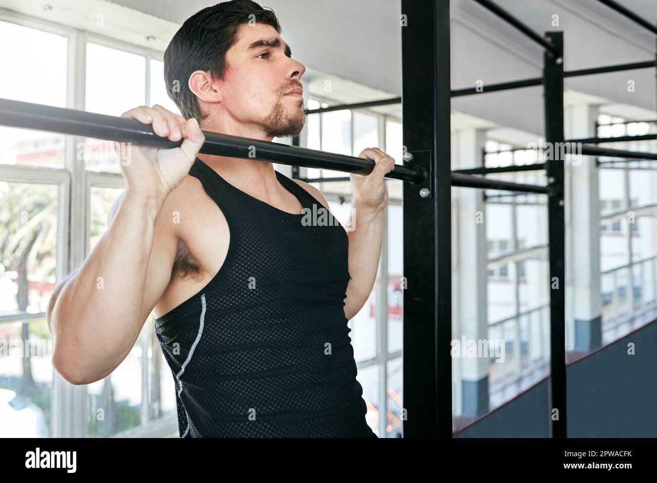 Sometimes the basic exercises are best. a young man doing pull ups in a gym. Stock Photo