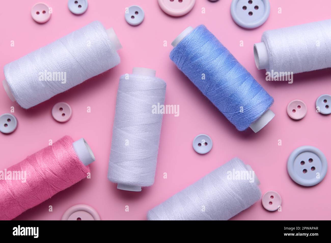 Composition with different thread spools and buttons on pink background, closeup Stock Photo