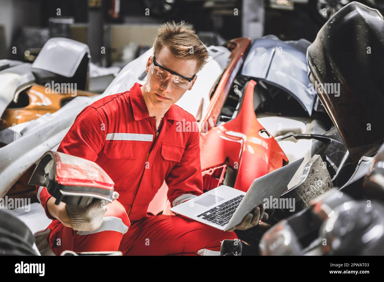 Old used car part warehouse worker checking inventory in garage. Staff worker working in recycle motor junkyard auto parts management. Stock Photo