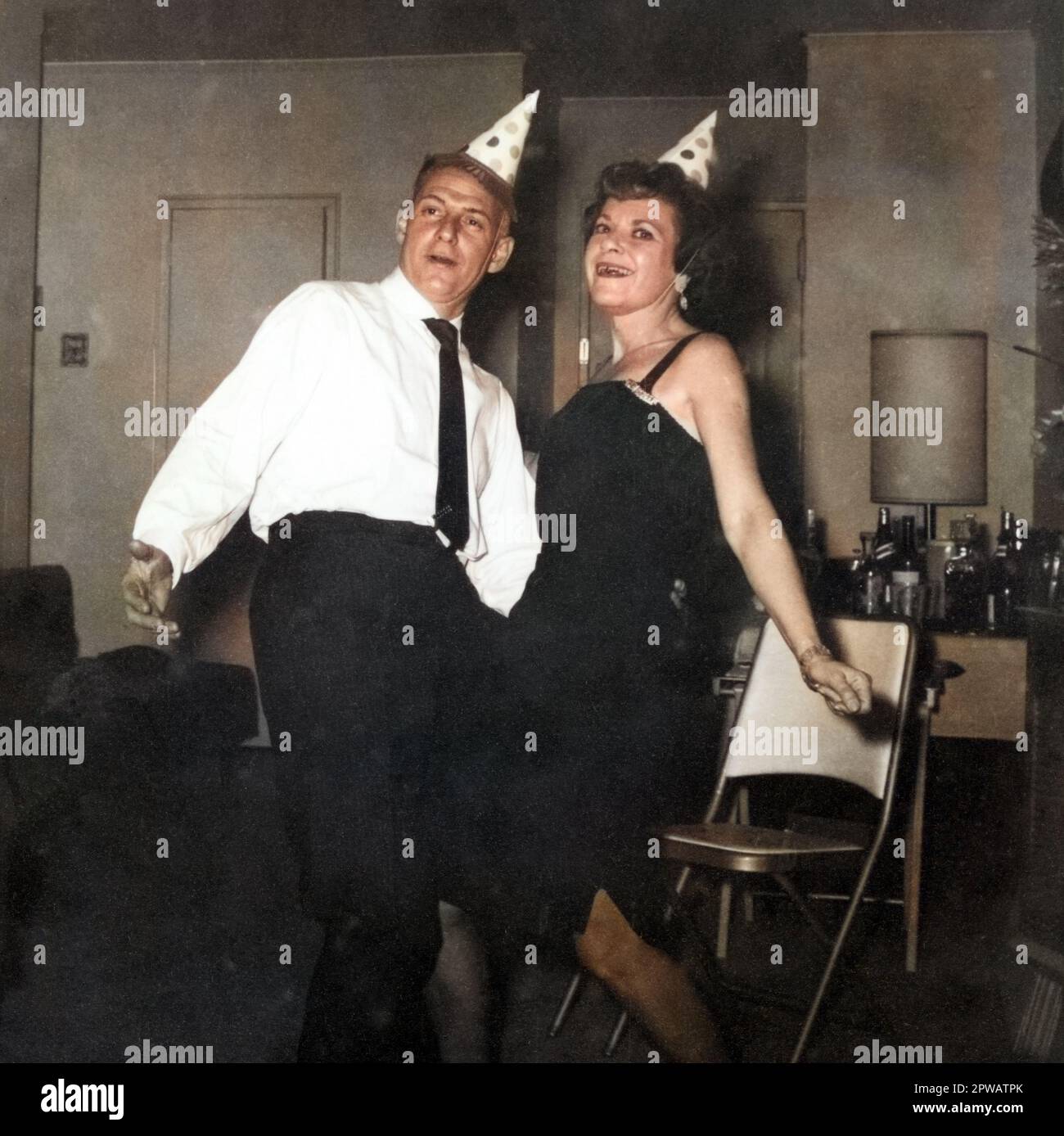 Archival photo of an adult couple dancing at home with party hats circa 1950s-1960s, likely New Year's Eve. Stock Photo