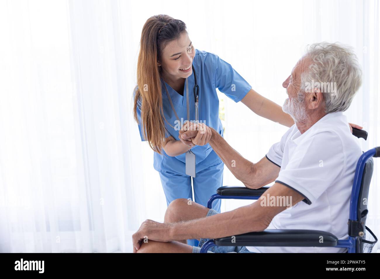 Homecare nurse staff take care elder male sitting at wheelchair happy smile together at home. Stock Photo