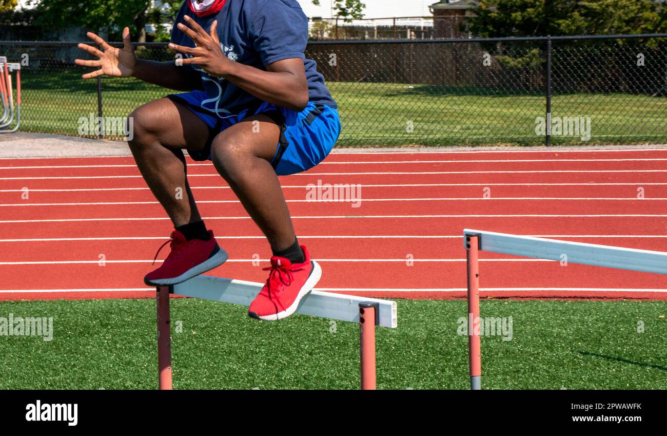 Side view of an African American male jumping over track hurdles at