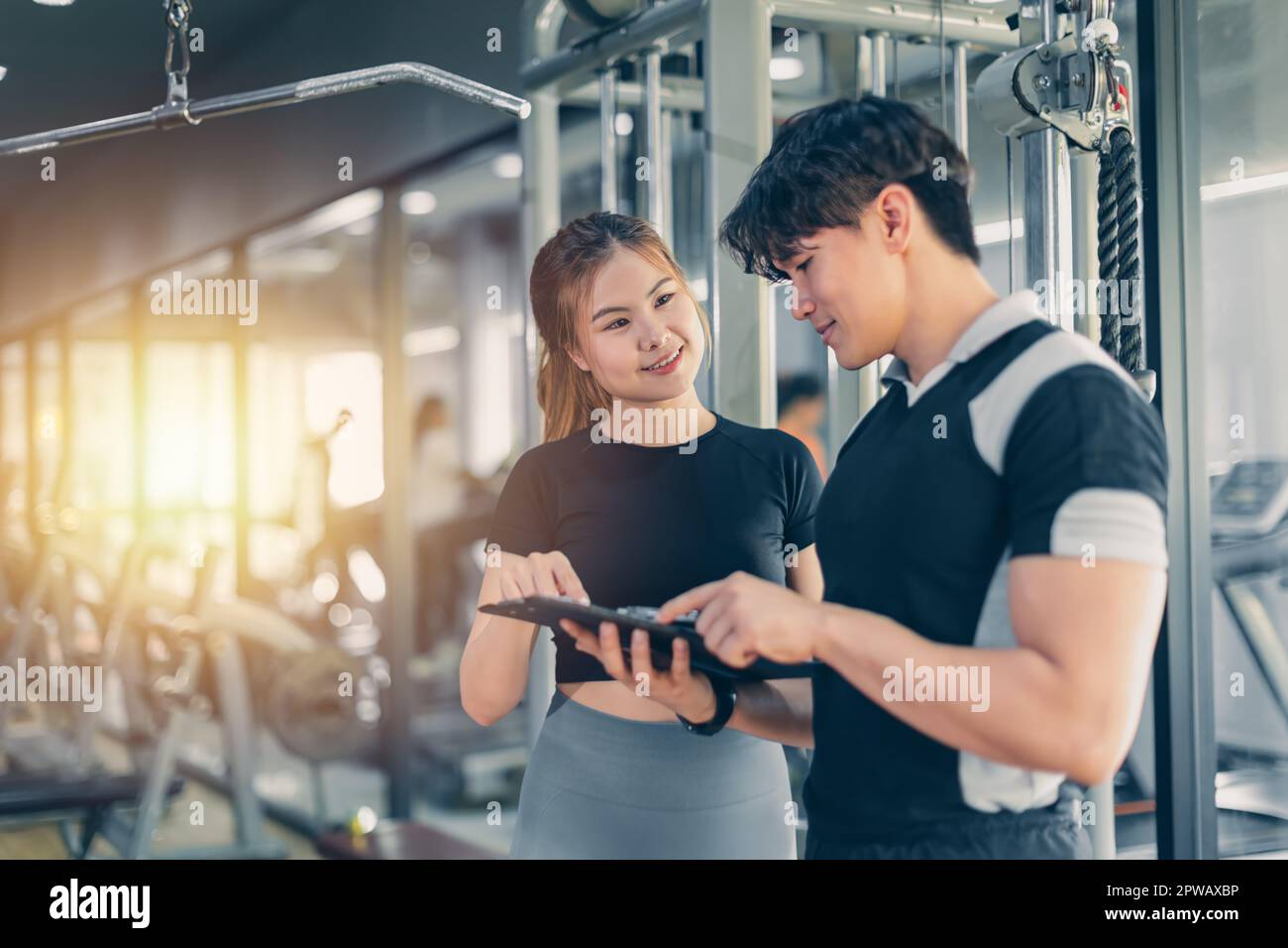 Fitness personal trainer talking with healthy lady customer about workout list weight training programs at the gym sport club Stock Photo