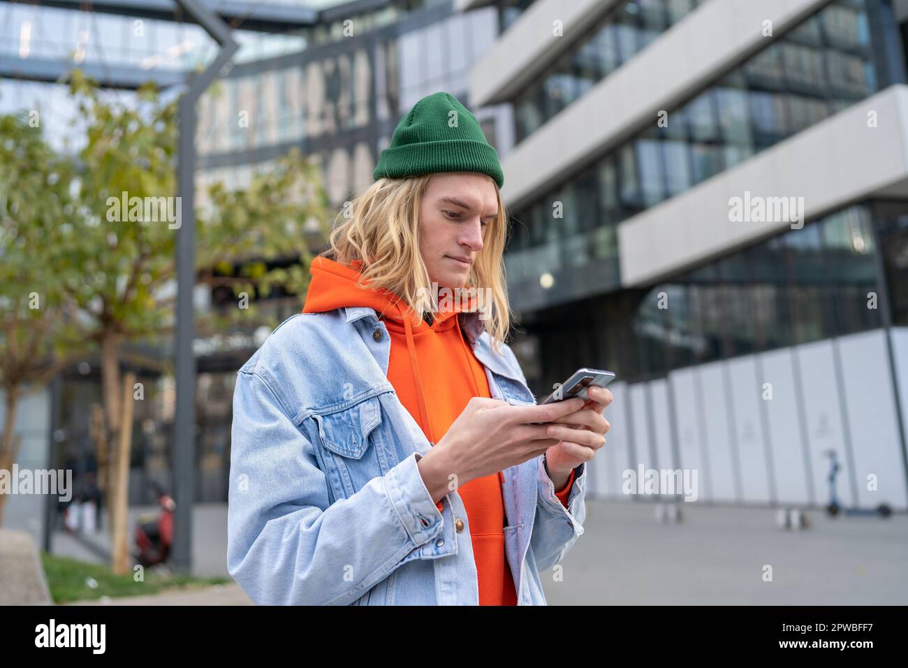 Millennial hipster guy browsing internet on mobile phone while standing on city street Stock Photo
