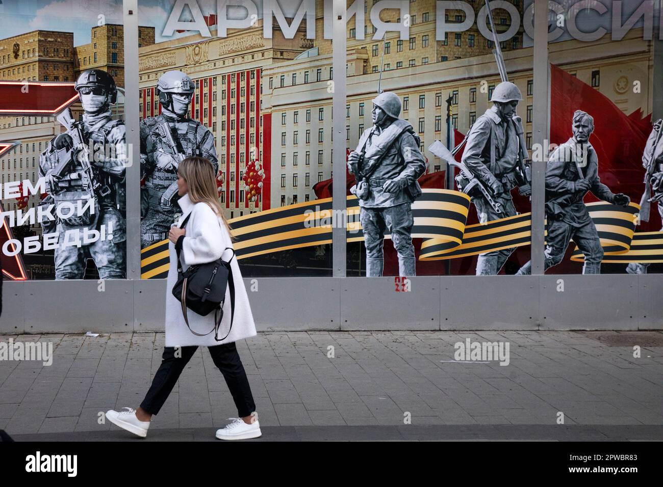 Moscow, Russia. 29th of April, 2023  A woman walks past the Army of Russia store with a festive banner for Victory Day celebration in the shop window in central Moscow, Russia. The banner reads 'Army of Russia!' Stock Photo