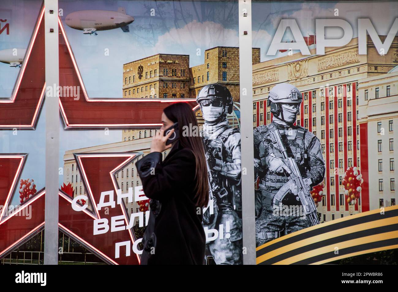 Moscow, Russia. 29th of April, 2023  A woman walks past the Army of Russia store with a festive banner for Victory Day celebration in the shop window in central Moscow, Russia. The banner reads 'Happy Great Victory Day!' Stock Photo