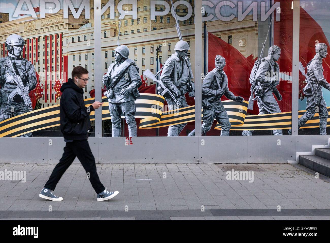 Moscow, Russia. 29th of April, 2023  A man walks past the Army of Russia store with a festive banner for Victory Day celebration in the shop window in central Moscow, Russia. The banner reads 'Army of Russia!' Stock Photo