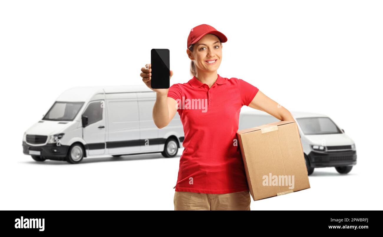 Female delivery worker in a red t-shirt holding a box and showing a mobile phone in front of transort vans isolated on white background Stock Photo