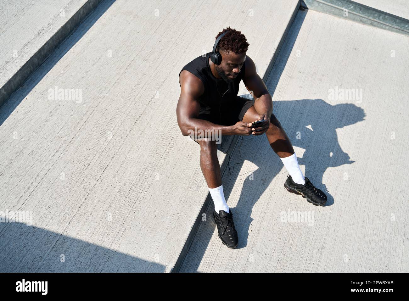 Fit sporty young black man using phone listening music during street workout. Stock Photo