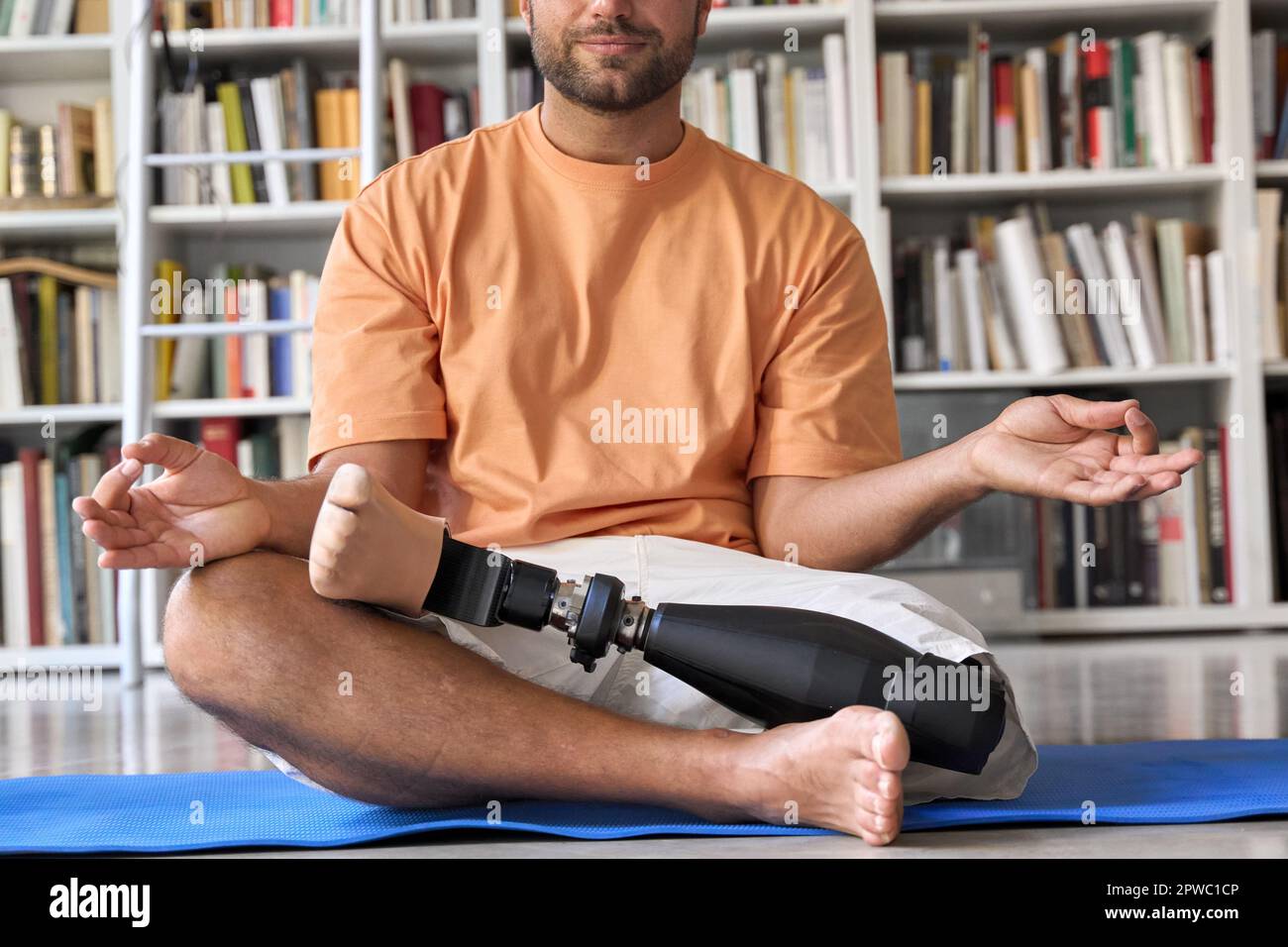 Amputee man with prosthetic leg prosthesis meditating doing yoga at home. Stock Photo