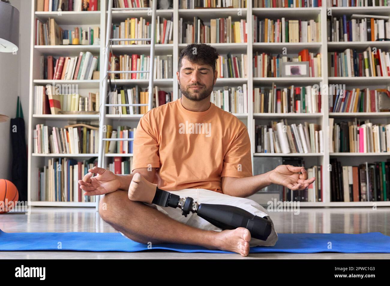 Amputee man with prosthetic leg prosthesis meditating doing yoga at home. Stock Photo