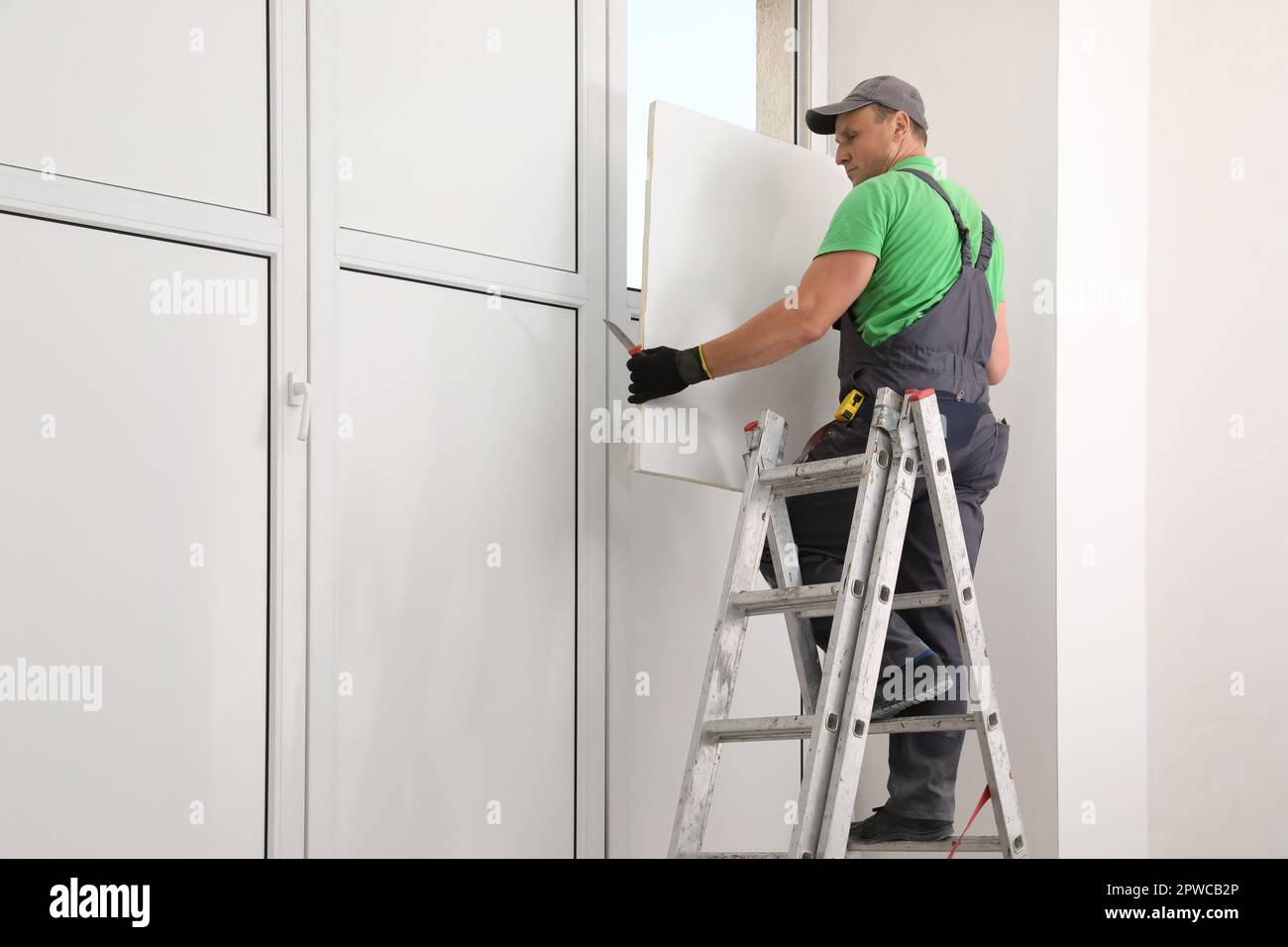 Worker on folding ladder installing window indoors Stock Photo