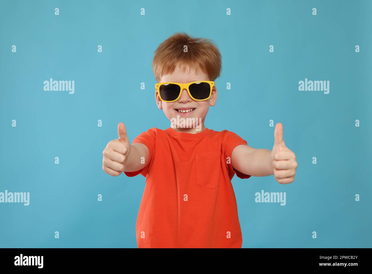 Cute little boy with sunglasses on light blue background Stock Photo