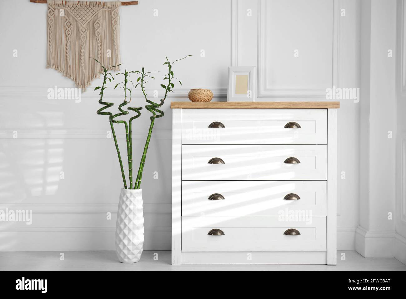https://c8.alamy.com/comp/2PWCBAT/vase-with-green-bamboo-stems-near-chest-of-drawers-in-room-interior-design-2PWCBAT.jpg