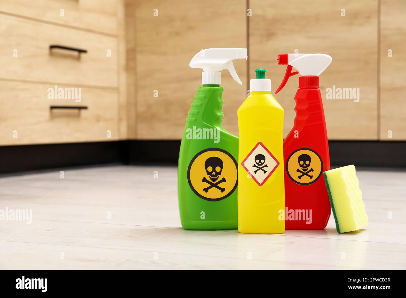 Bottles of toxic household chemicals with warning signs and scouring sponge on floor indoors