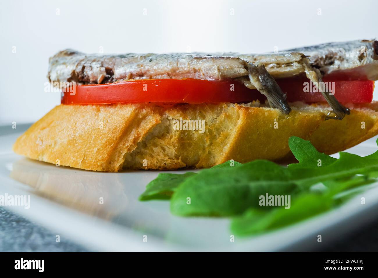 Tapa of sardines on a slice of bread with tomato and olives on a white