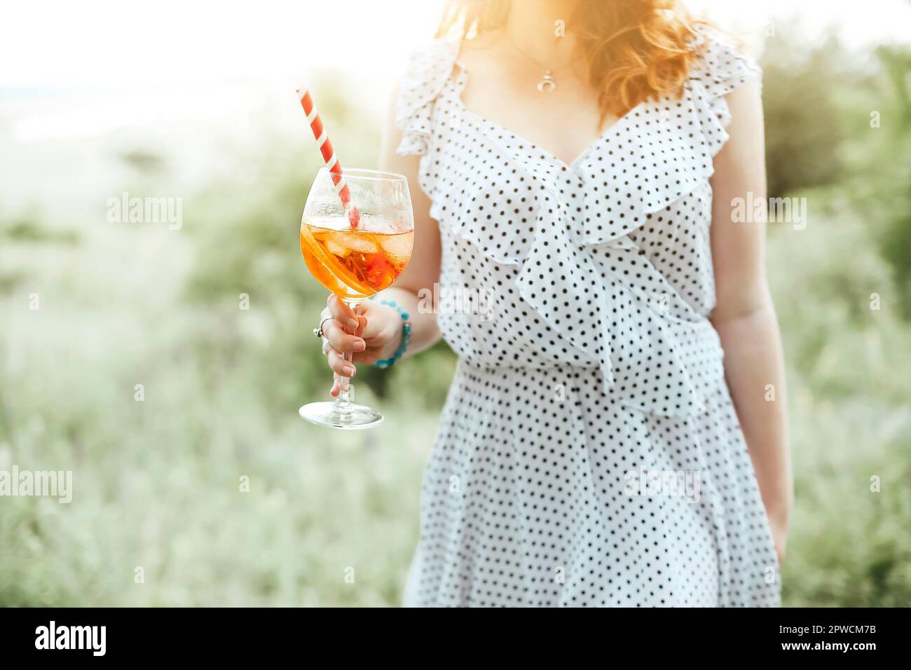 Young female drinking alcohol cocktail with orange on blurred background of nature Stock Photo