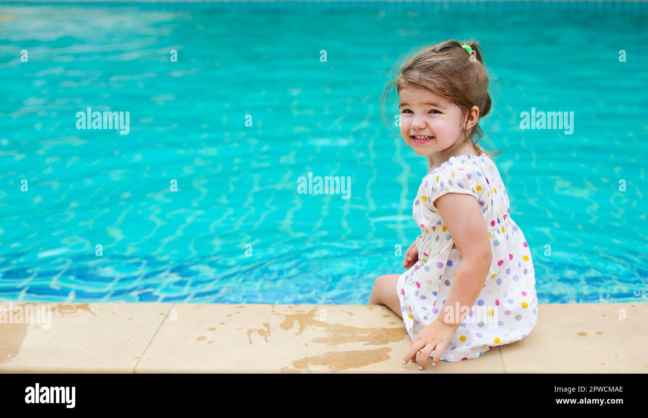 Back view of delighted kid in dress sitting near swimming pool and