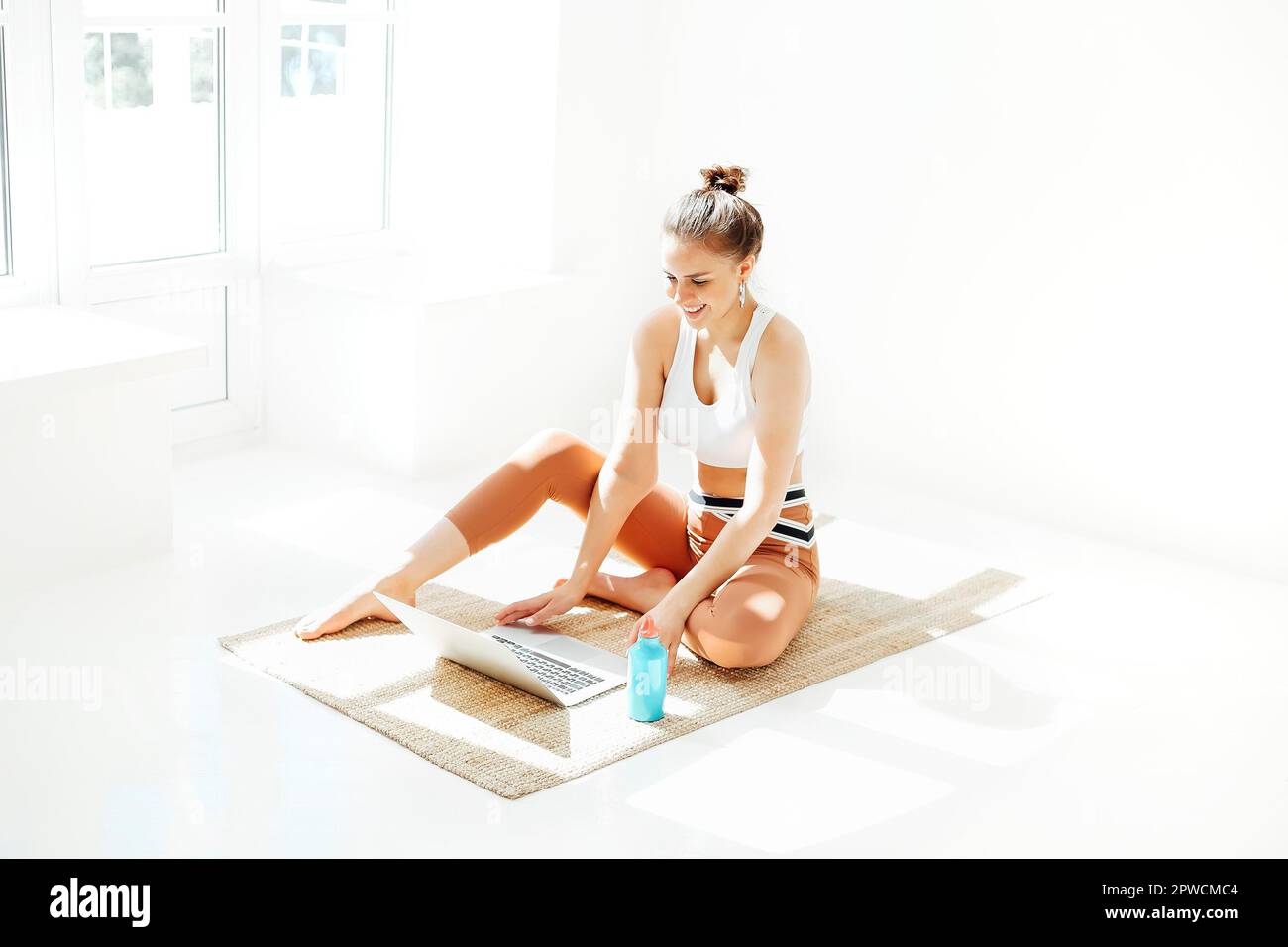 Slim young female in sportswear watching video on laptop while practicing yoga near the window at home Stock Photo