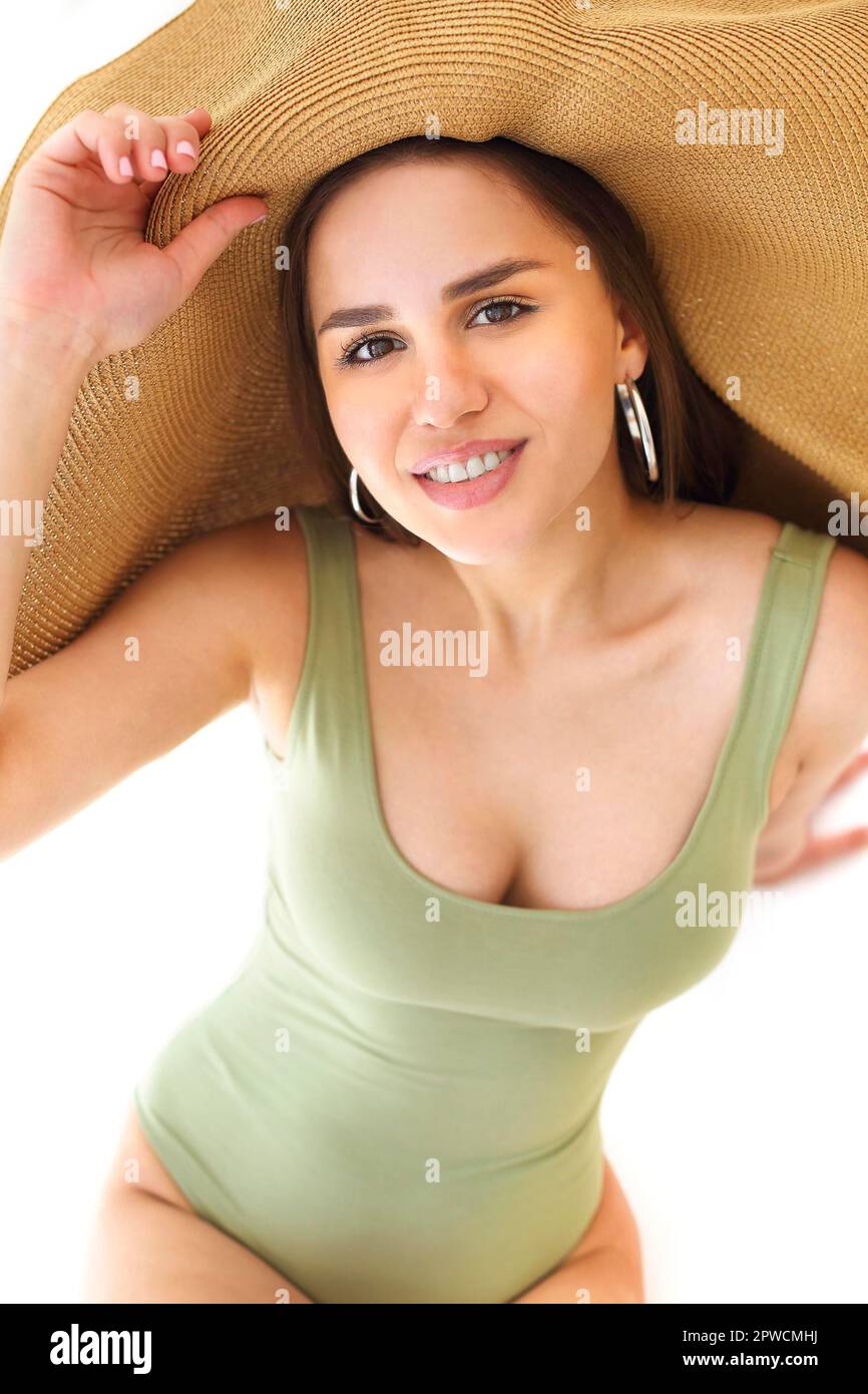 Young female in green swimsuit and stylish summer hat covering face against white background Stock Photo