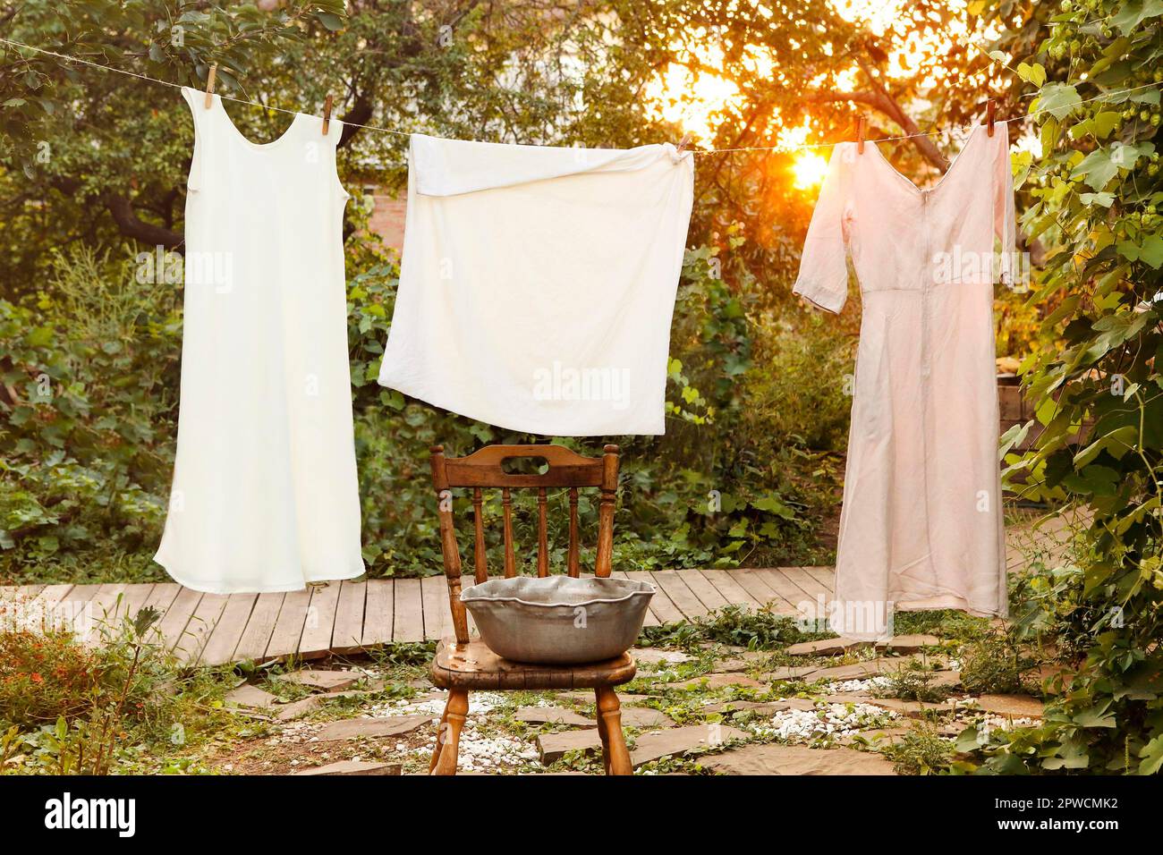 Clean wet garments hanging on rope and drying near retro chair and bowl on laundry day in garden Stock Photo