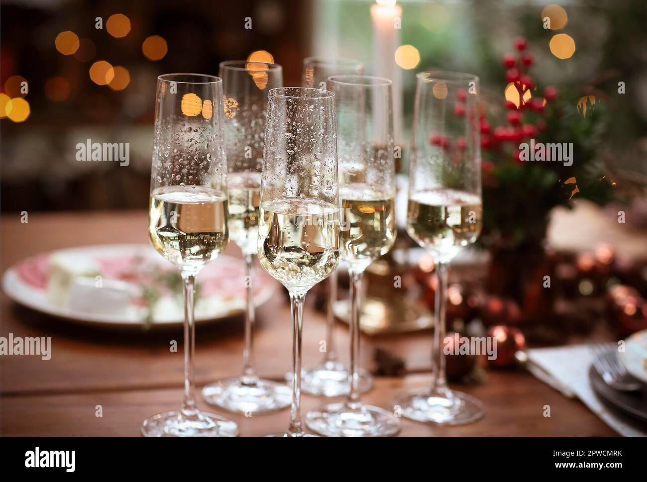 Set of champagne glasses on wooden table with candles against blurred wall with Christmas tree Stock Photo