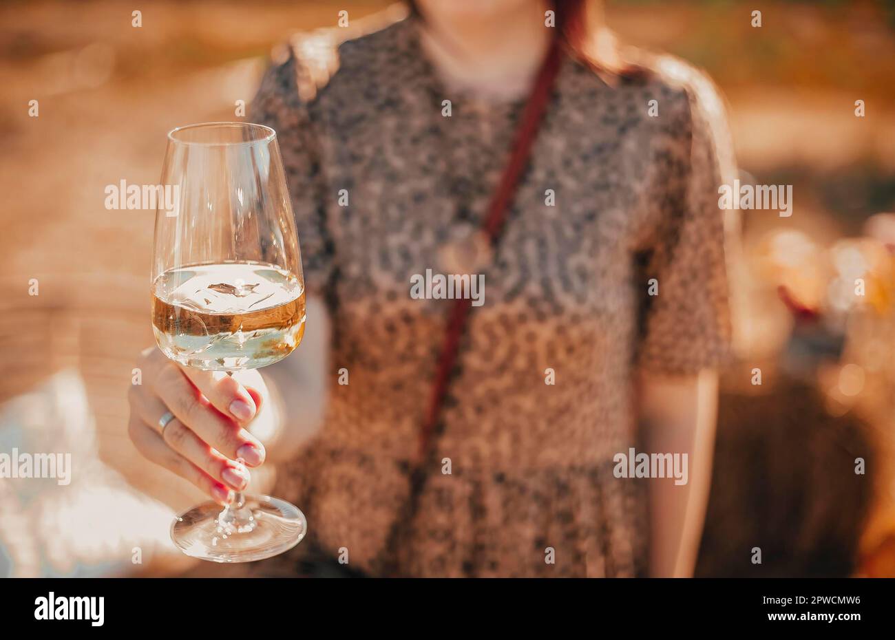 Unrecognizable female in floral dress enjoying white wine on sunny summer day in nature Stock Photo