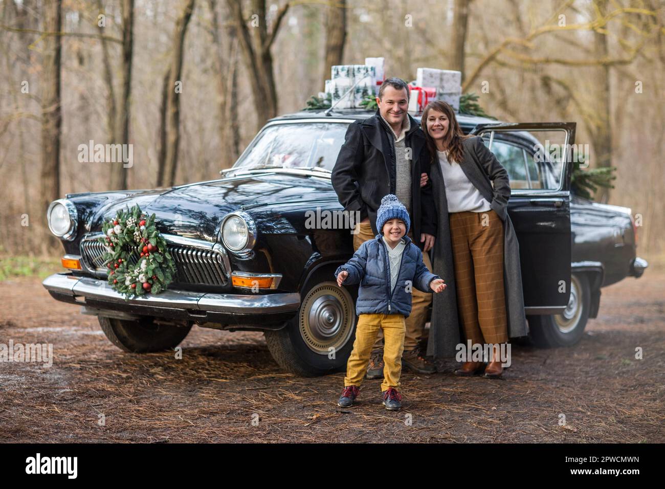 Smiling adult man and woman with boy in warm clothes standing at vintage car with Christmas presents Stock Photo
