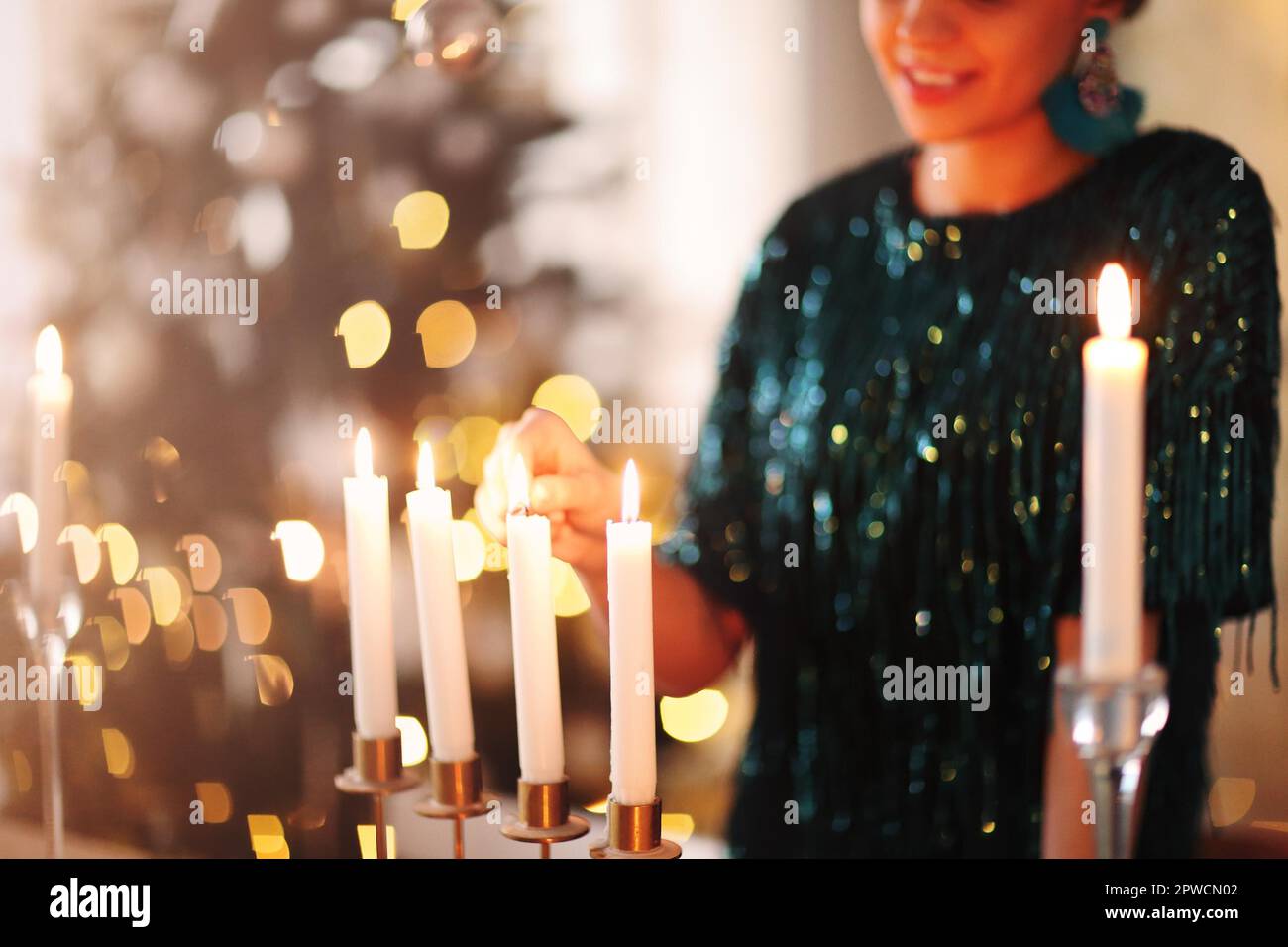Unrecognizable female smiling and igniting candles while creating romantic mood in evening at home Stock Photo