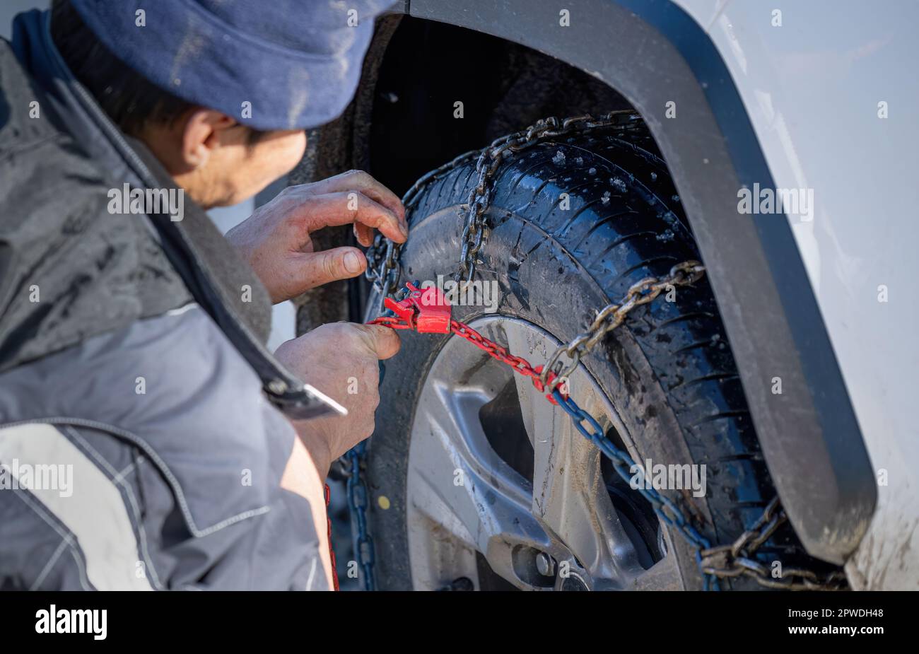 Man putting snow chains on his car wheels to improve traction in the winter weather condition. Stock Photo
