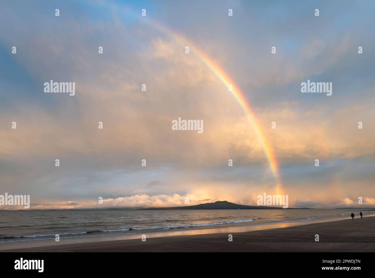 Rainbows over Rangitoto Island. Unrecognizable people walking on Milford beach. Auckland. Stock Photo