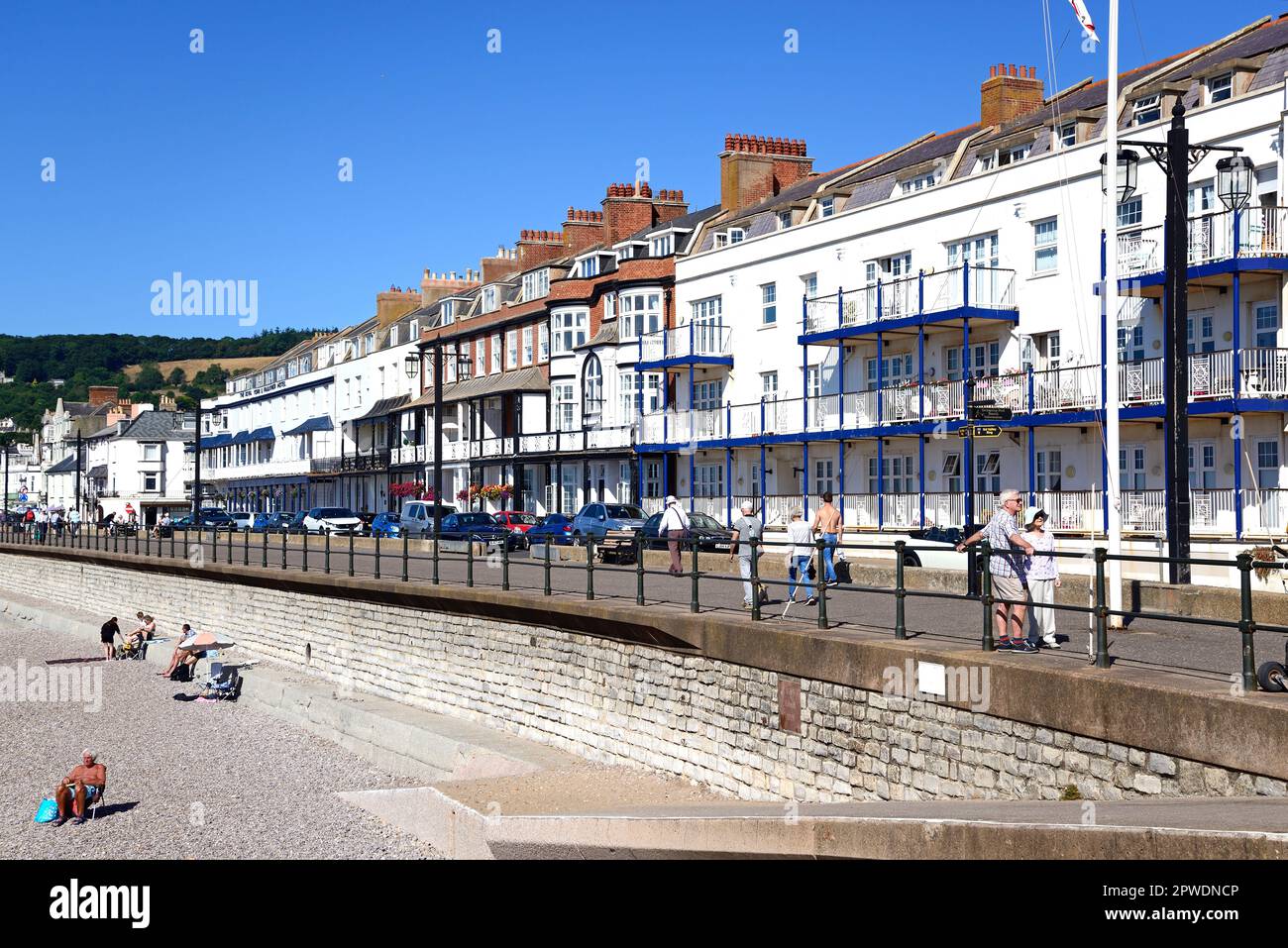 View of hotels along the promenade seen from the beach with tourists enjoying the setting, Sidmouth, Devon, UK. Stock Photo