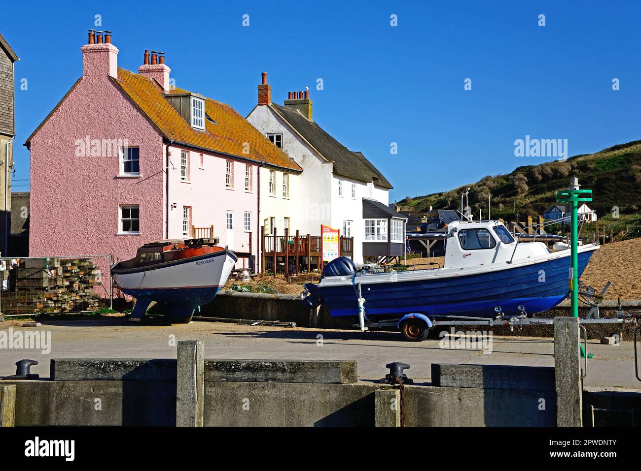 Fishing boats in dry dock with pretty beachside cottages to the rear, West Bay, Dorset, UK, Europe. Stock Photo