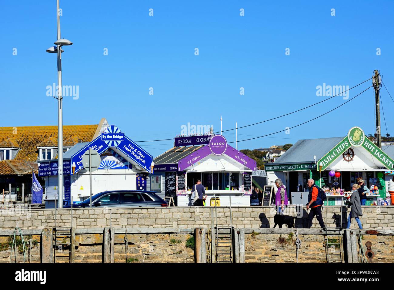 Tourists looking at snack kiosks alongside the harbour in the town, West Bay, Dorset, UK, Europe. Stock Photo