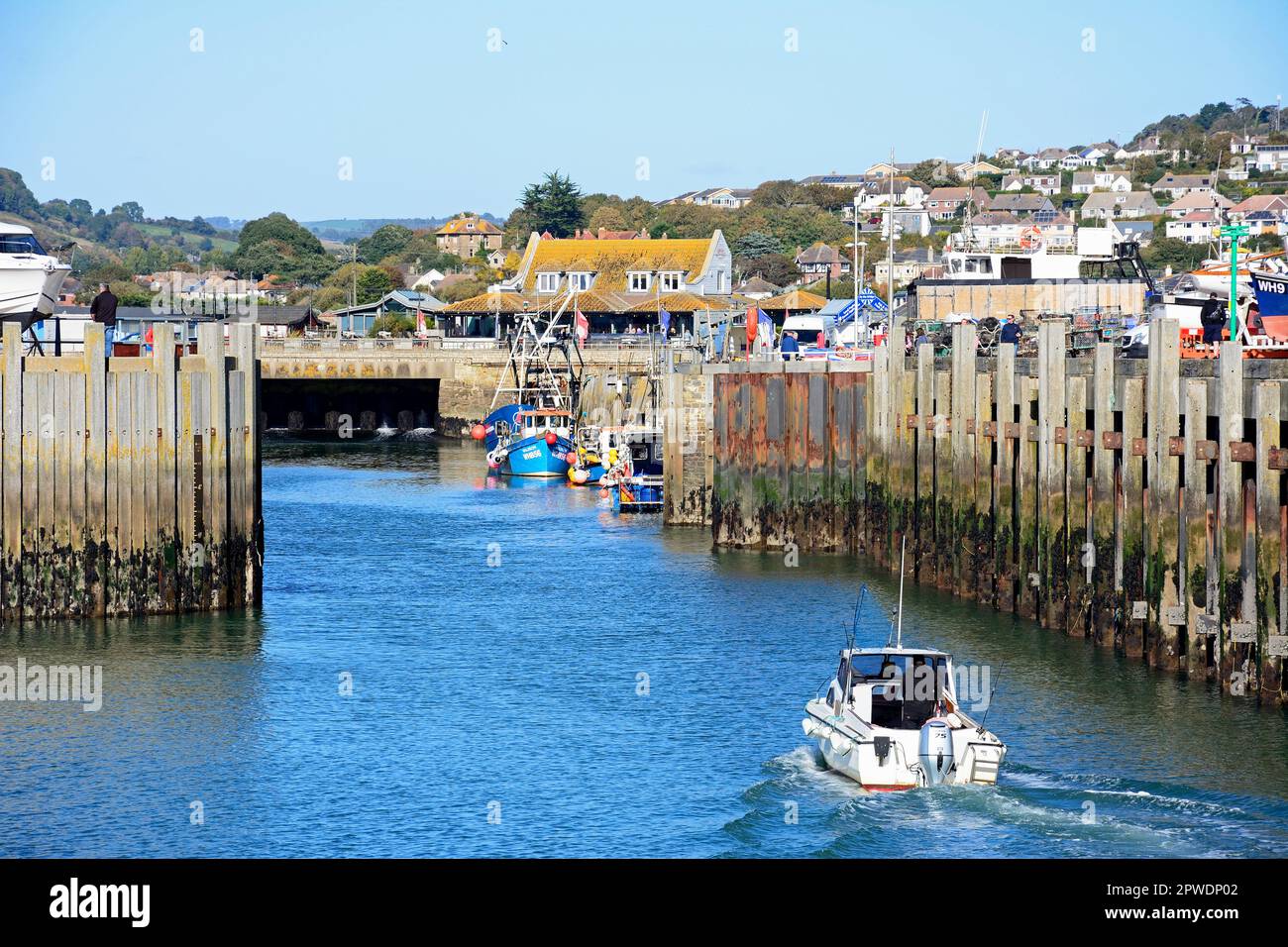 Boat entering the harbour with the sluice gate and town buildings to the rear, West Bay, Dorset, UK, Europe. Stock Photo
