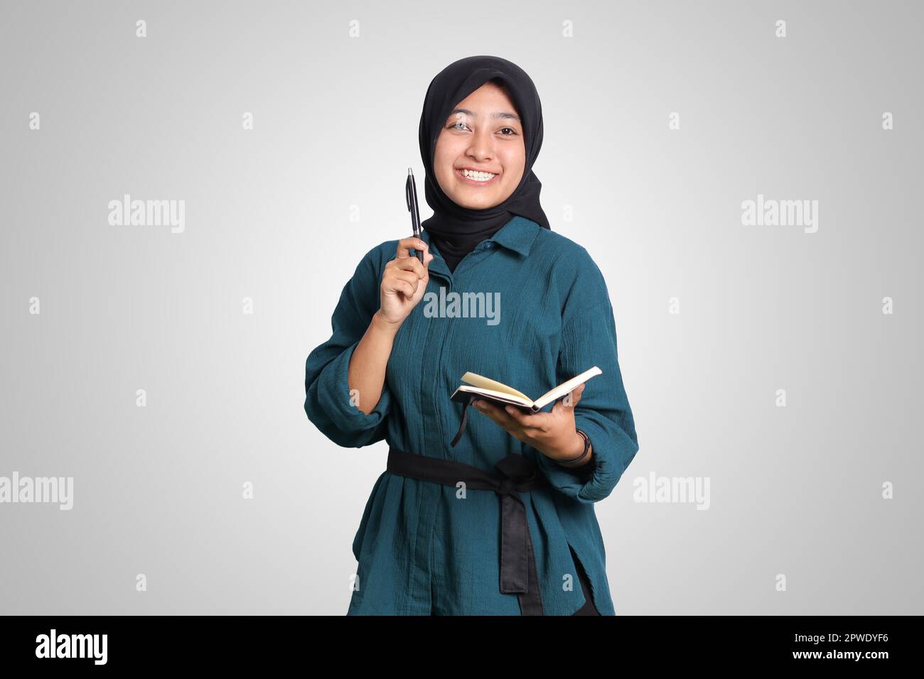 Portrait of excited Asian muslim woman with hijab writing on note book ...