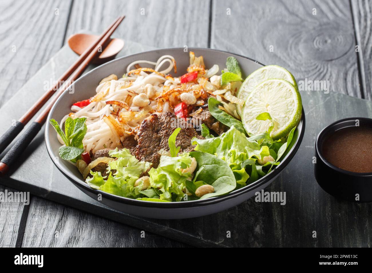 Pho Bo Tron Mixed beef noodles salad is a popular dish in Vietnamese cuisine closeup on the bowl on a wooden table. Horizontal Stock Photo