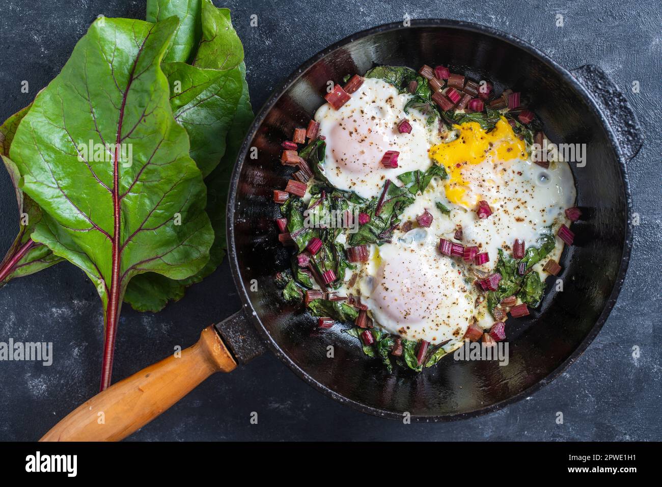 Fried eggs with green beet leaves, onion, pepper and spices in cast iron pan, close up, top view Stock Photo