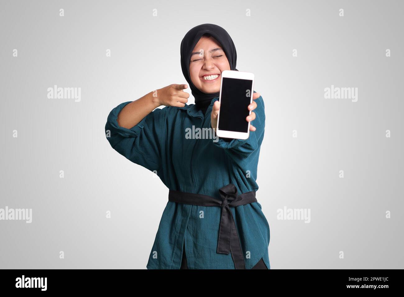 Portrait of excited Asian muslim woman with hijab showing and presenting blank screen mobile phone. Advertising mock up concept. Isolated image on whi Stock Photo