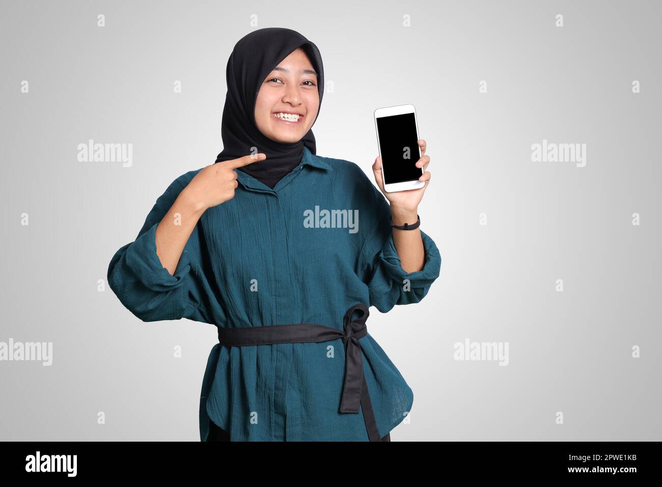 Portrait of excited Asian muslim woman with hijab showing and presenting blank screen mobile phone. Advertising mock up concept. Isolated image on whi Stock Photo