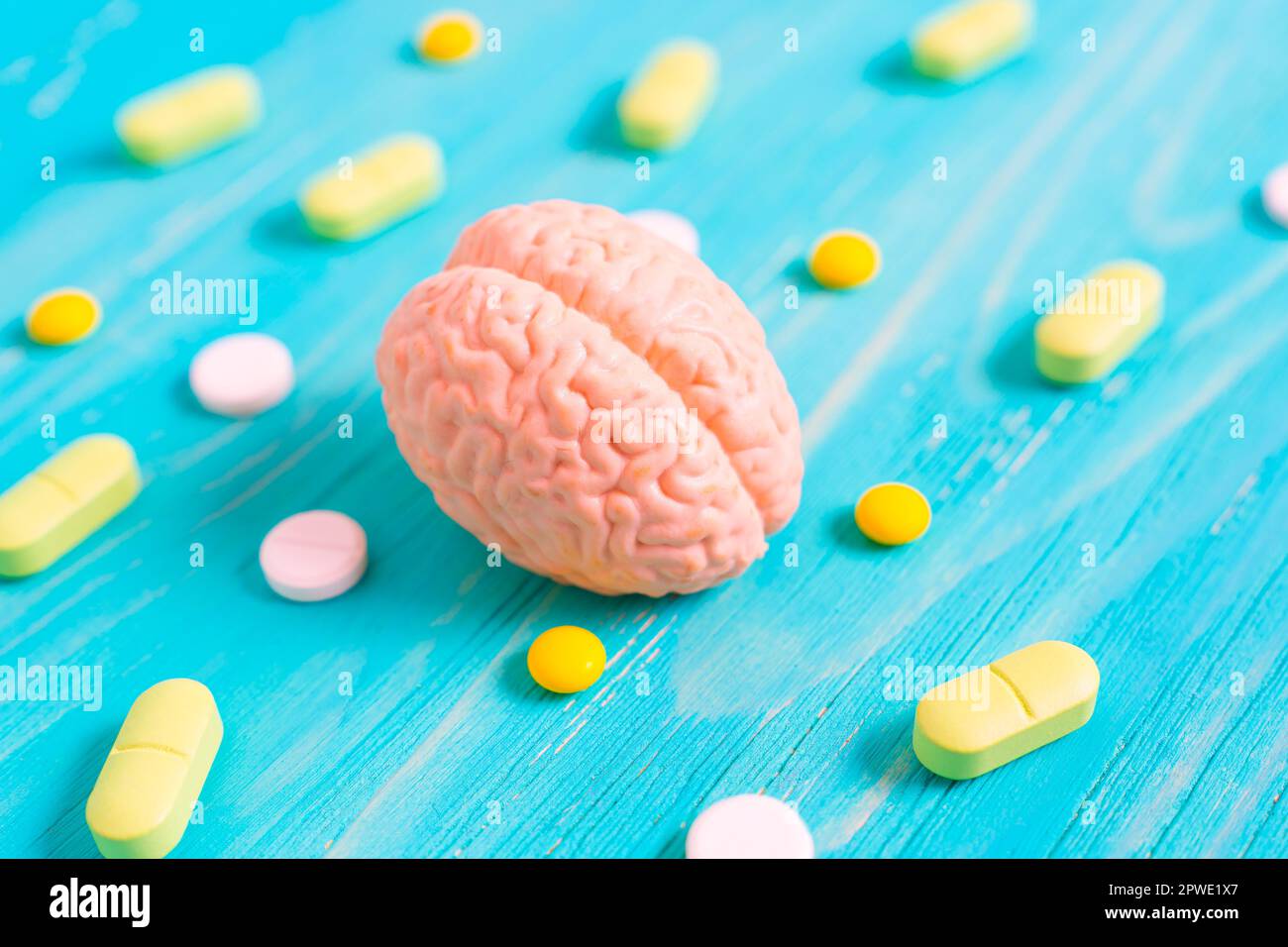 Miniature human brain model alongside scattered yellow and white pills on a blue wooden table. Brain function, medication, treatment and preserving co Stock Photo