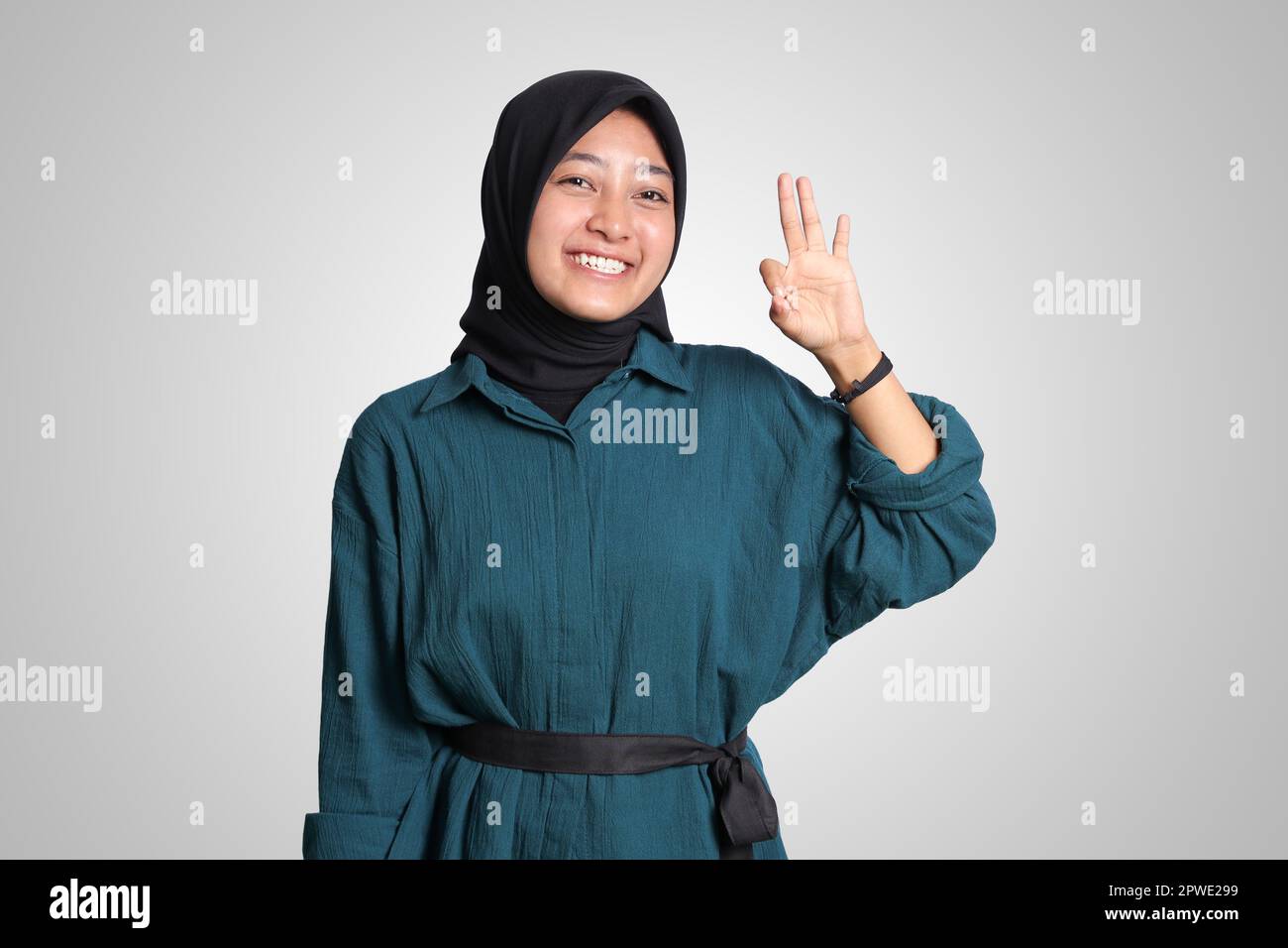 Portrait of excited Asian muslim woman with hijab showing ok hand gesture and smiling looking at camera. Advertising concept. Isolated image on white Stock Photo