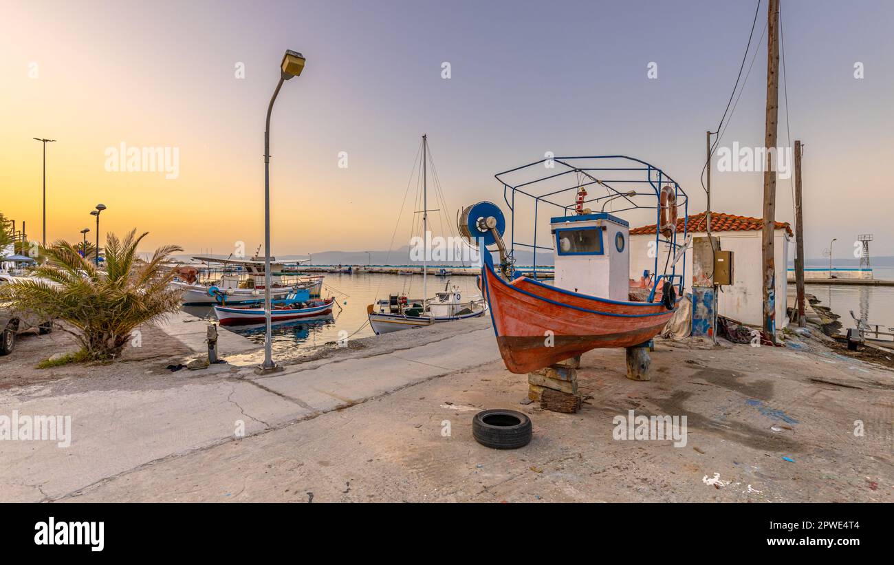 Fishing harbor scene in Greece with boats, palm trees and scooters at sunrise on a beautiful tranquil summer day Stock Photo