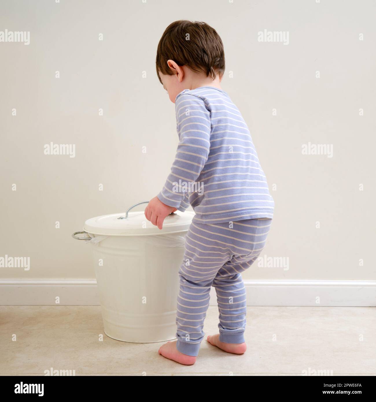 Toddler baby throws garbage in the trash can. A happy child lifts the