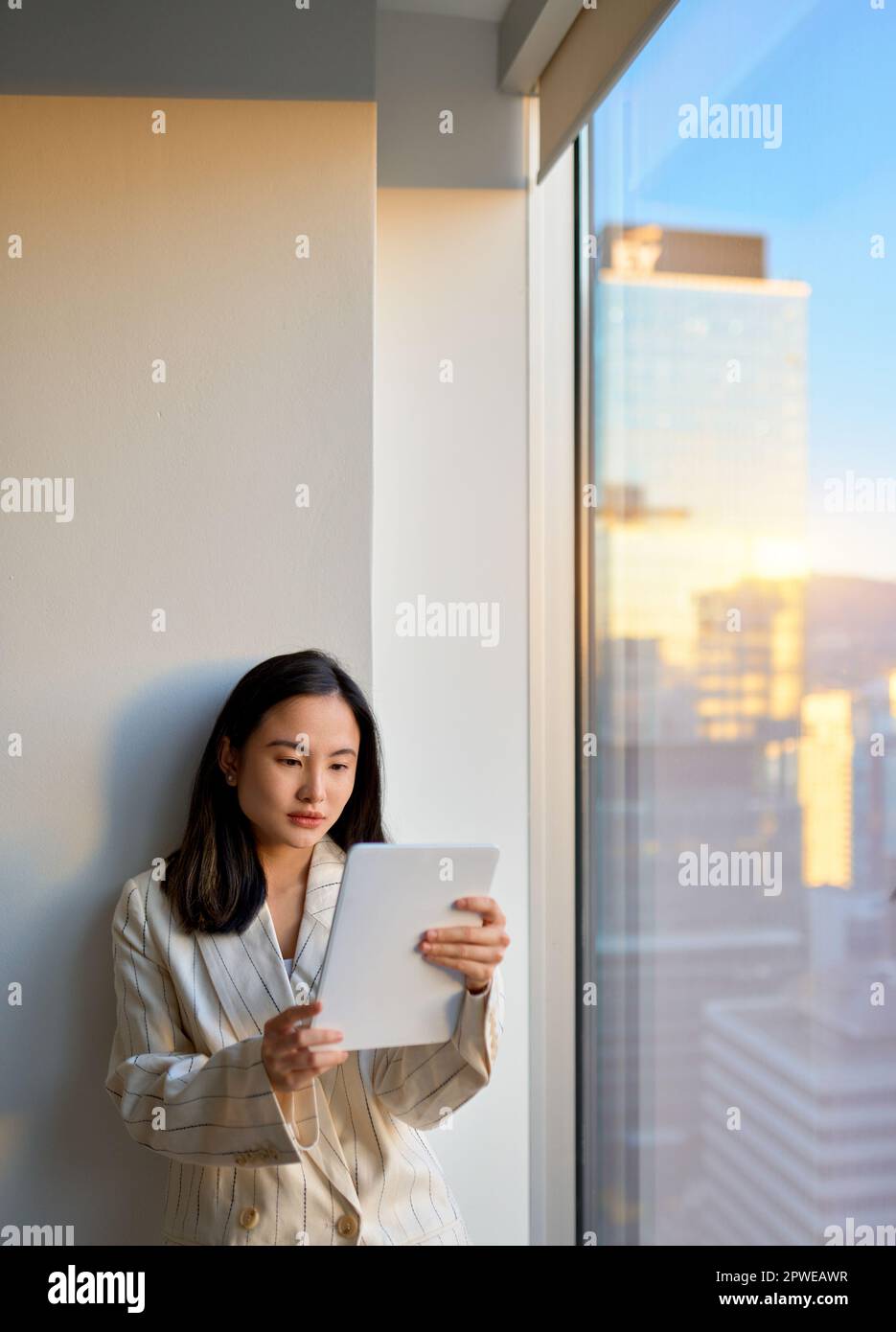Young Asian business woman using digital tablet standing at office window. Stock Photo