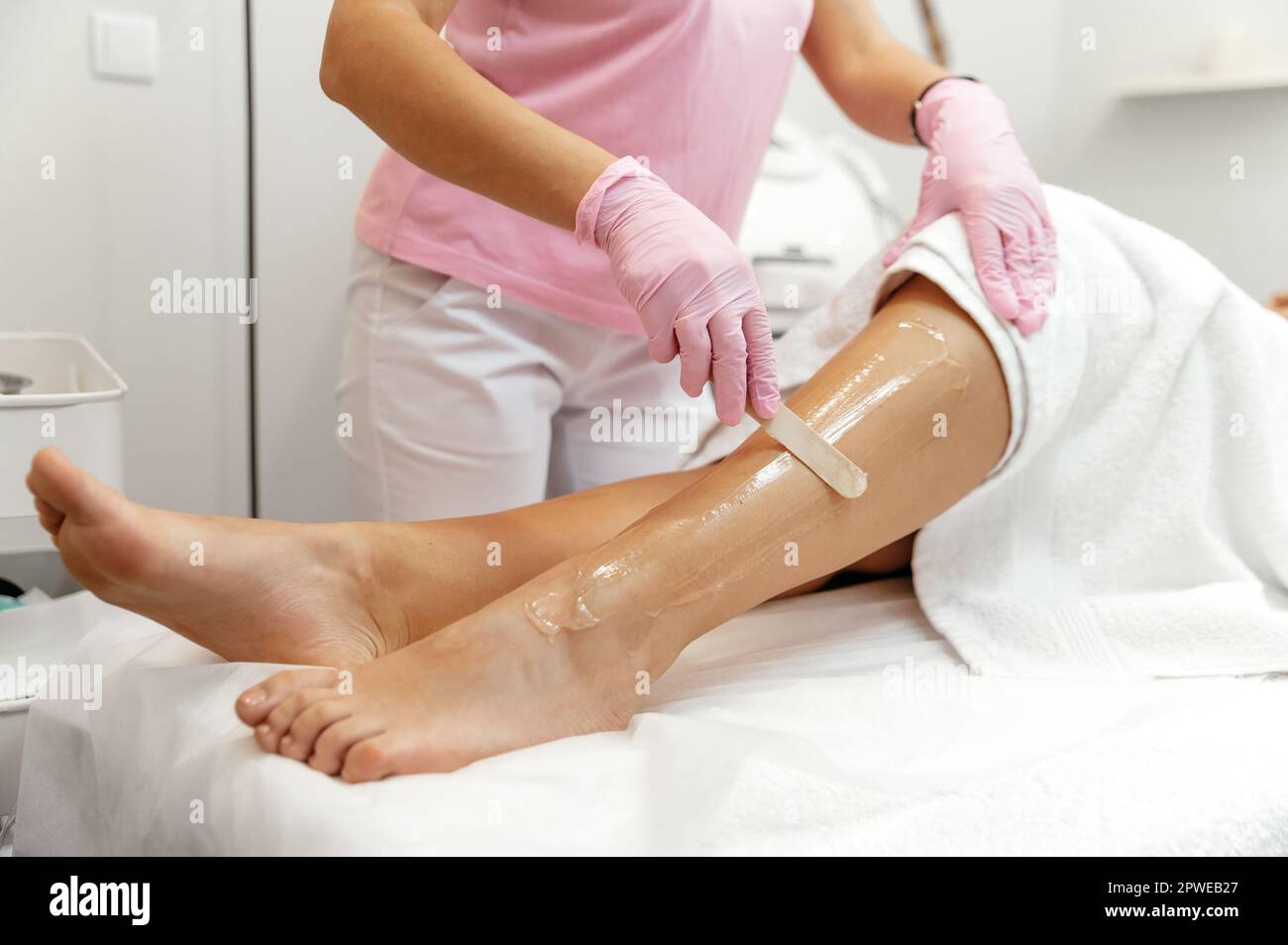 Hair removal cosmetology procedure. Aesthetic cosmetology. Laser epilation and cosmetology. Cosmetologist prepares leg before laser hair removal, applies gel on leg Stock Photo