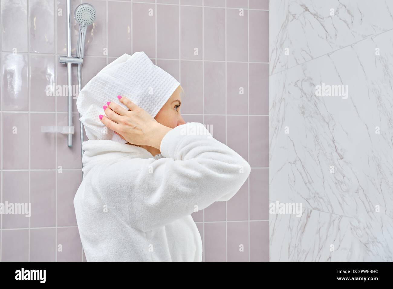 Middle aged woman in bathrobe wrapping her hair in towel after shower
