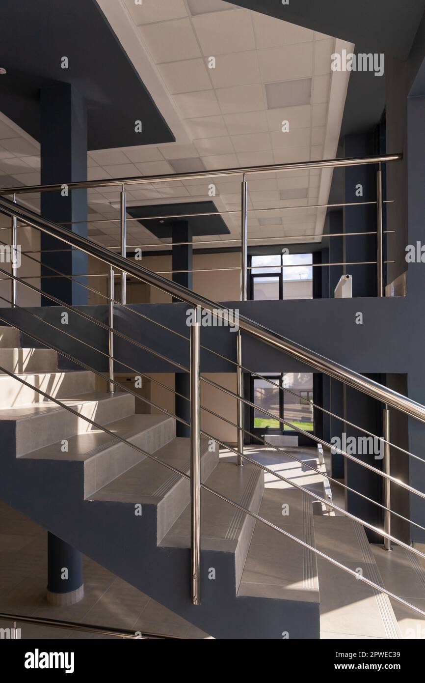 Stairs in a concrete office building in neutral tones, covered with ceramic tiles, with shiny metal railings made of stainless steel, extensive glazin Stock Photo