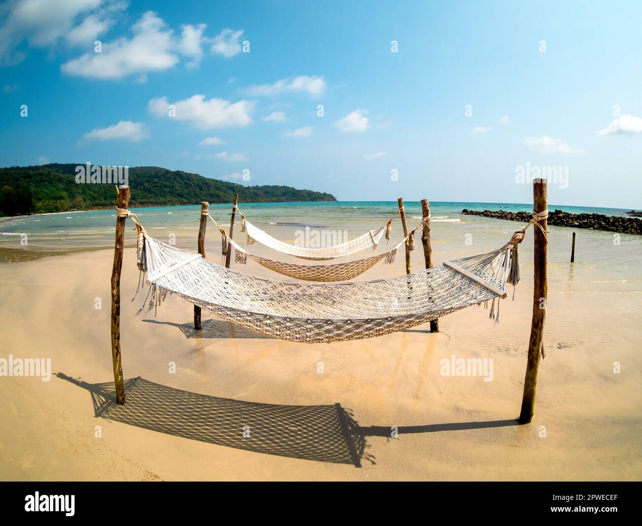 Three empty rope cradle hanging on the wooden poles on sandy beach on